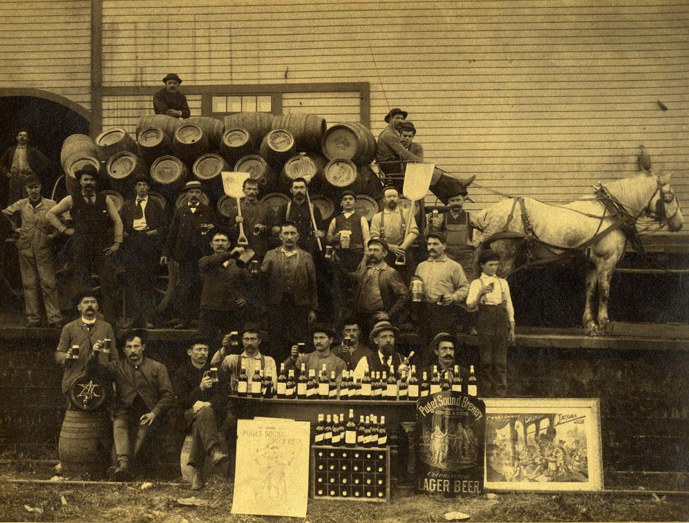 Group photo of employees of the Puget Sound Brewing Company in front of a wood frame building. 